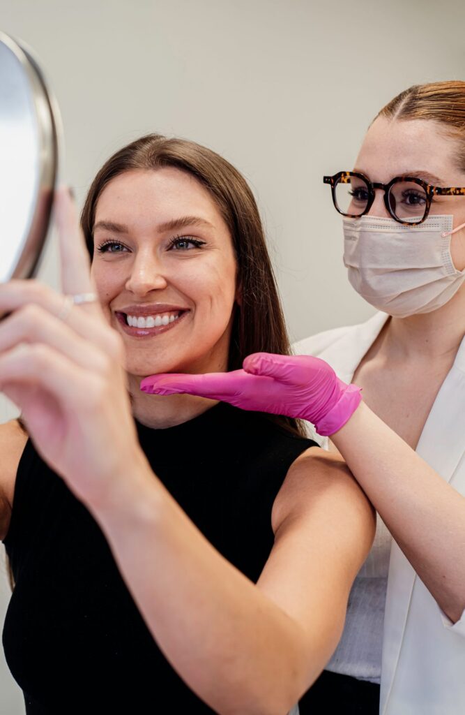 Smiling woman looking in a hand mirror during a beauty clinic visit with a provider nearby