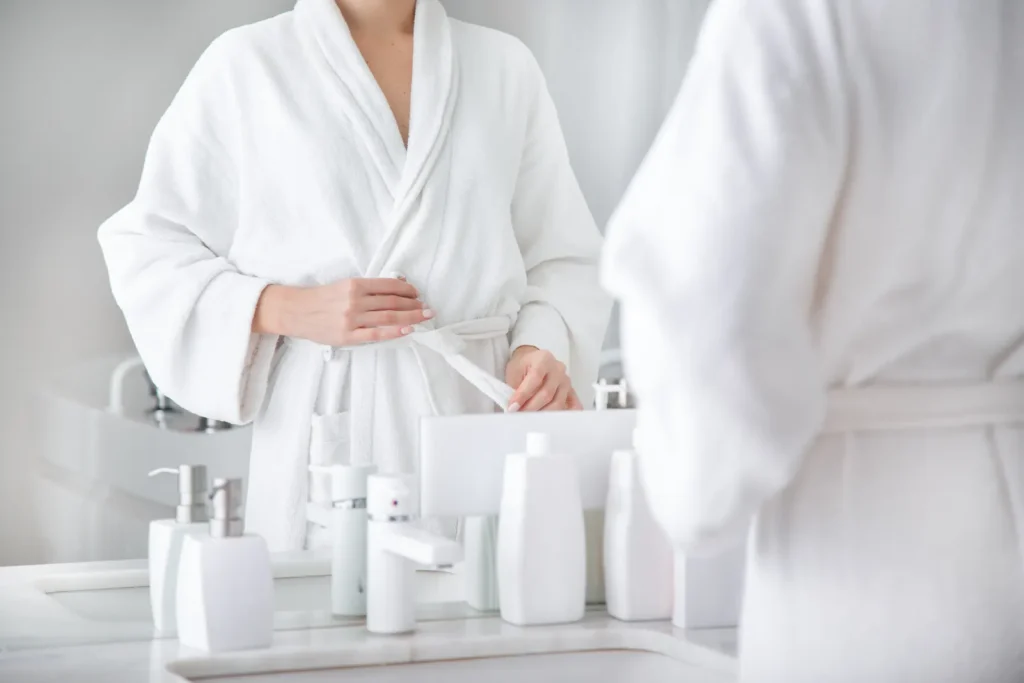 Woman tying the belt of a white robe in a bright bathroom
