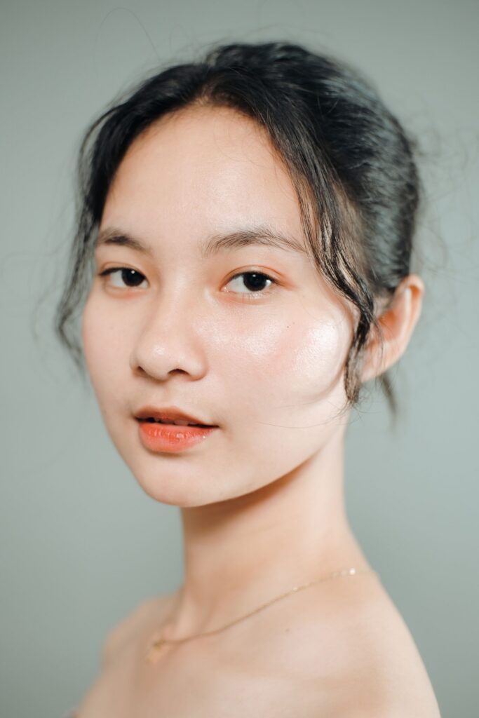 Close portrait of a young woman with dark hair pulled back and a calm expression, in front of a soft sage-green background
