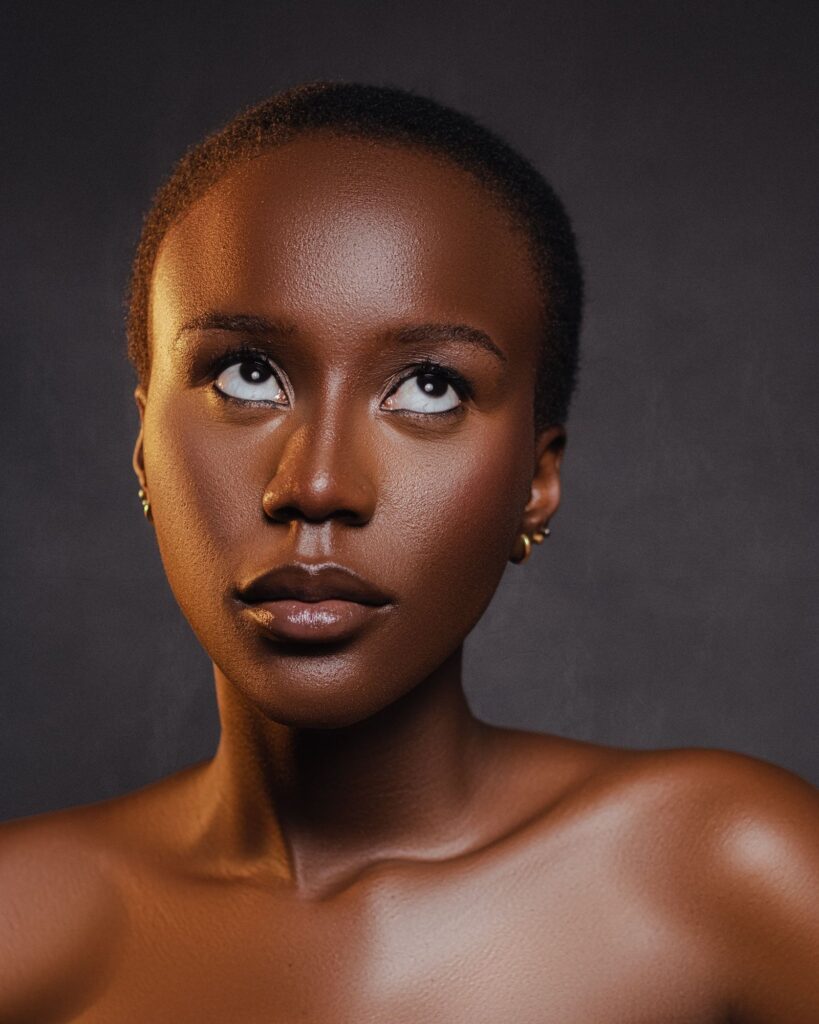 Studio portrait of a woman with short dark hair and a deep skin tone, looking upward in front of a dark grey background