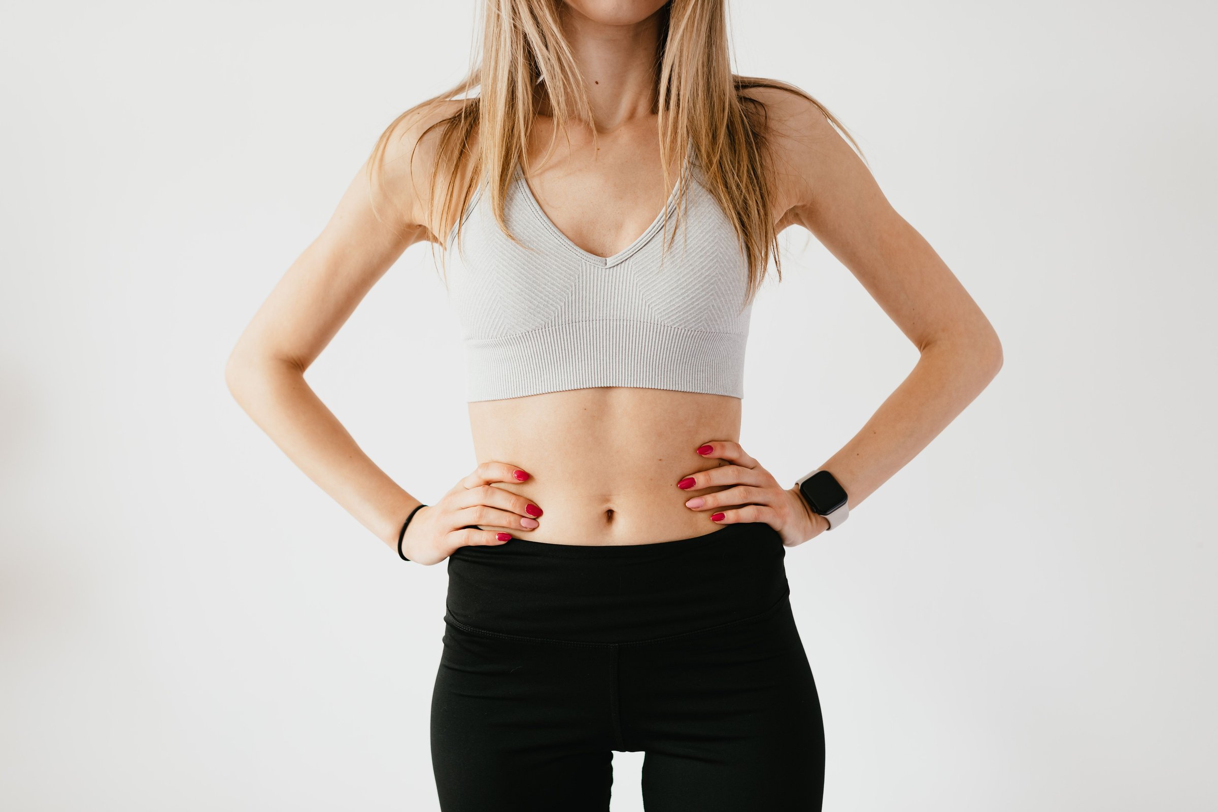 Woman in a gray sports bra and black leggings with hands on her waist, illustrating tummy tuck candidacy in Newport Beach