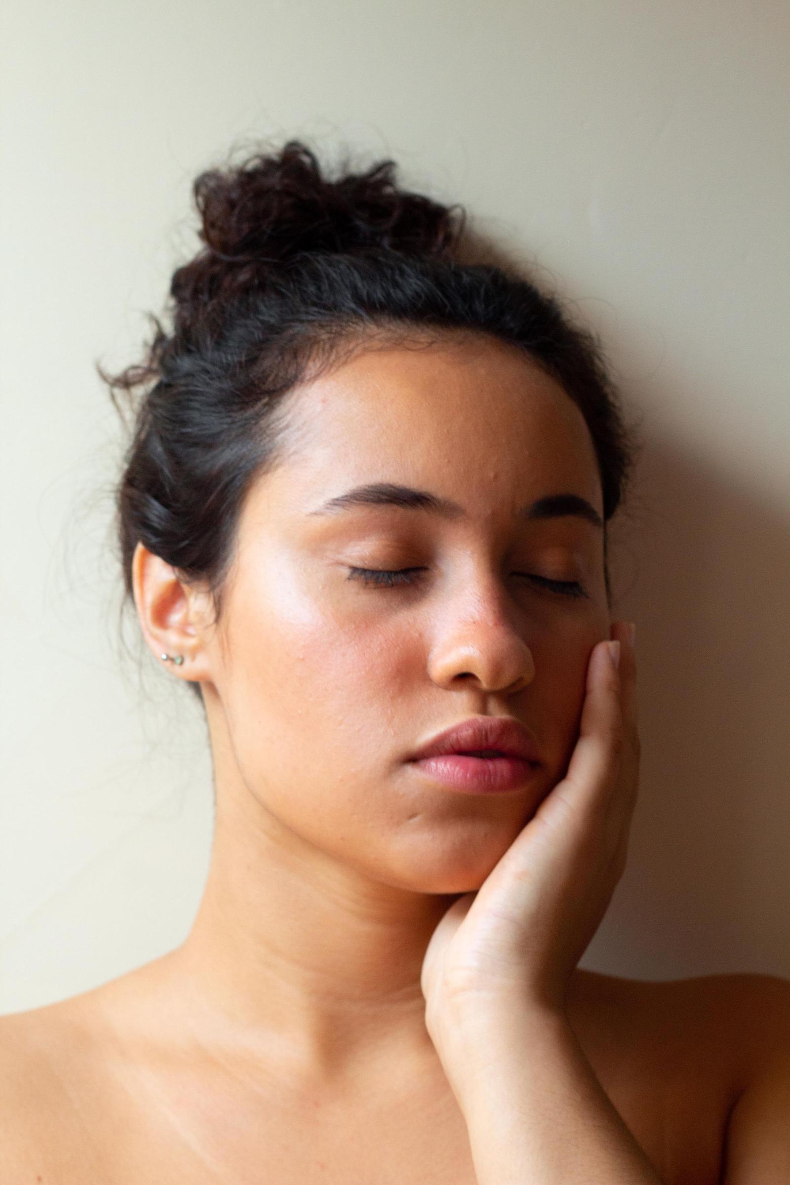 Calm woman with eyes closed resting her hand on her cheek, with smooth, even-toned skin