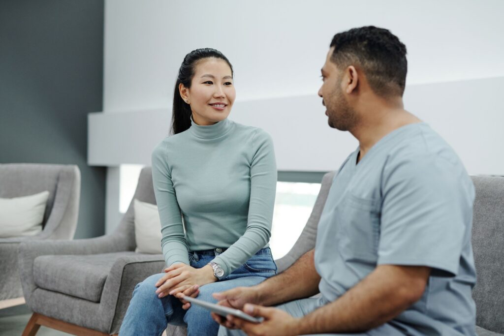 Clinician holding a tablet while talking with a smiling woman seated in a bright, modern clinic