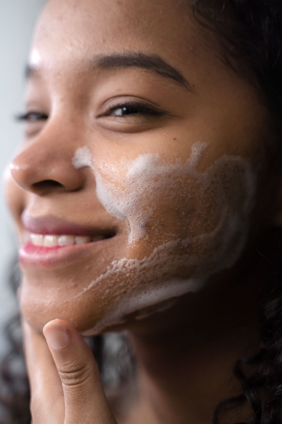 Smiling woman with glowing skin rinsing a gentle cleanser from her face