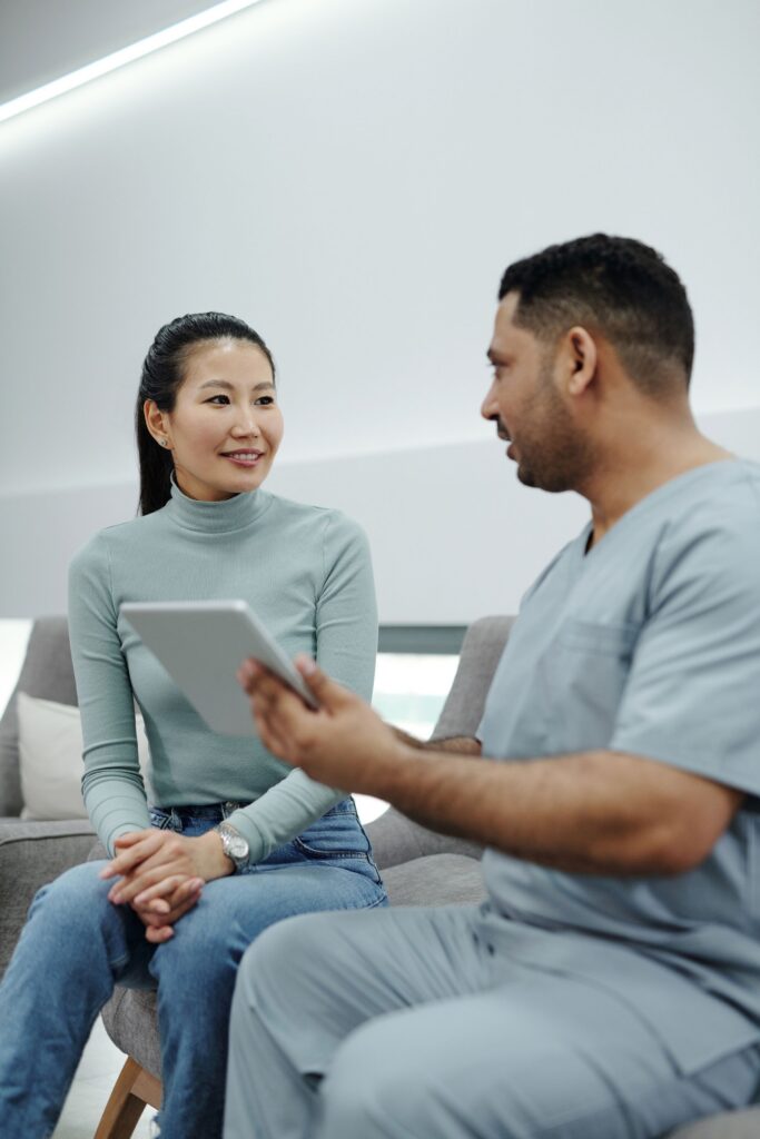 Smiling woman seated beside a man in scrubs who holds a tablet while they talk