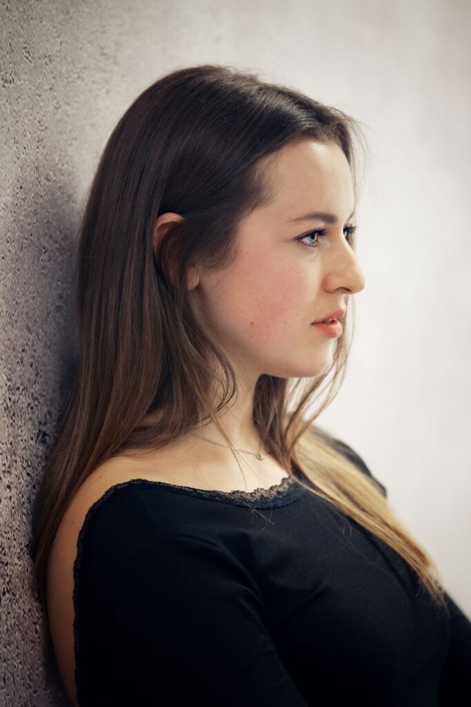 Profile portrait of a young woman against a textured wall, showing the line of the cheek and jaw