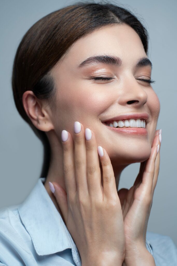 Smiling woman with closed eyes and hands resting on her cheeks, showing radiant, healthy-looking skin