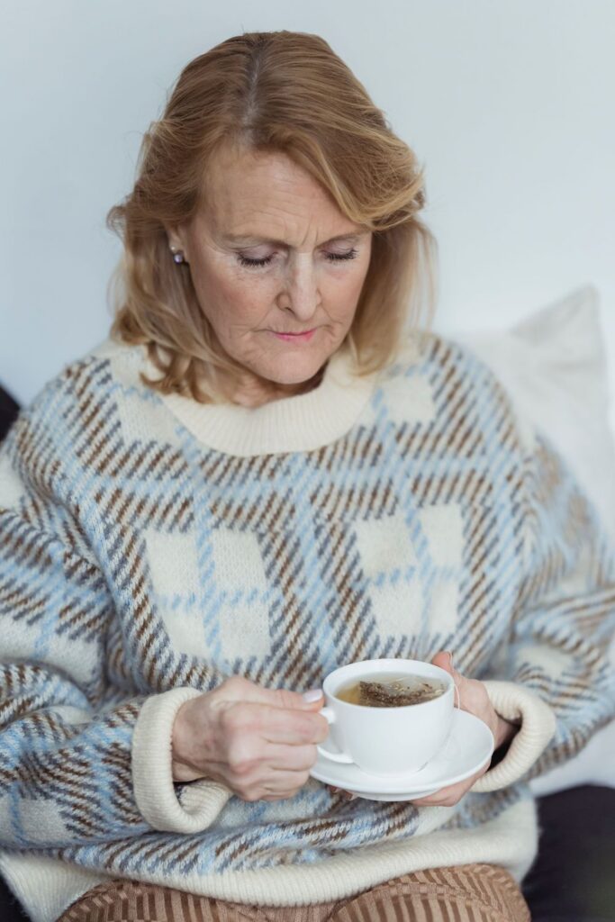 Woman in a blue and cream patterned sweater holding a cup of tea on a saucer, looking down